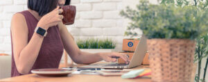 A woman working from a laptop and drinking coffee.