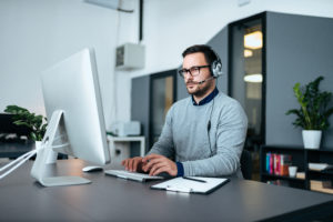 Young male customer support with headset working on the computer.